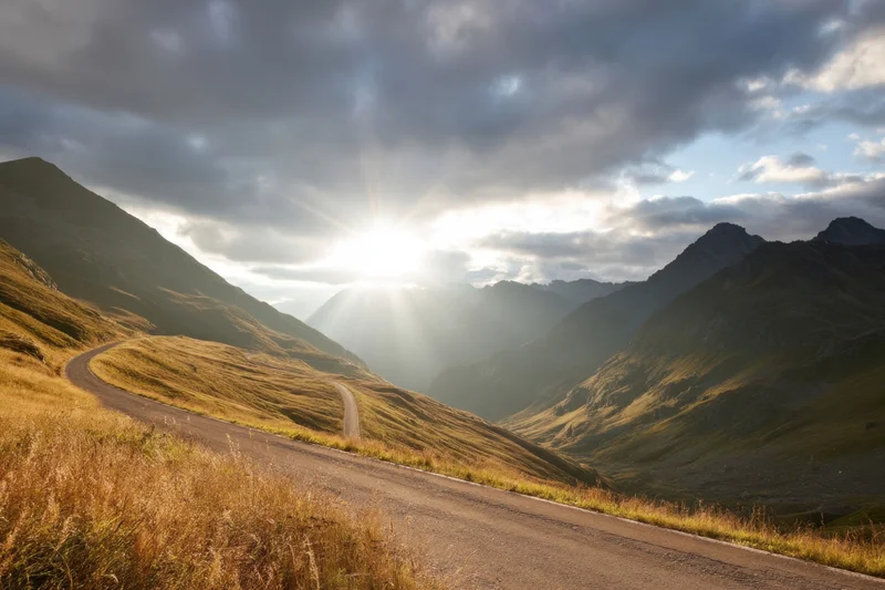 Winding mountain road through sunlit alpine valley