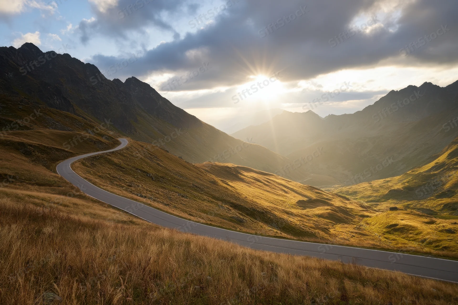 Winding mountain road through sunlit alpine valley at sunset