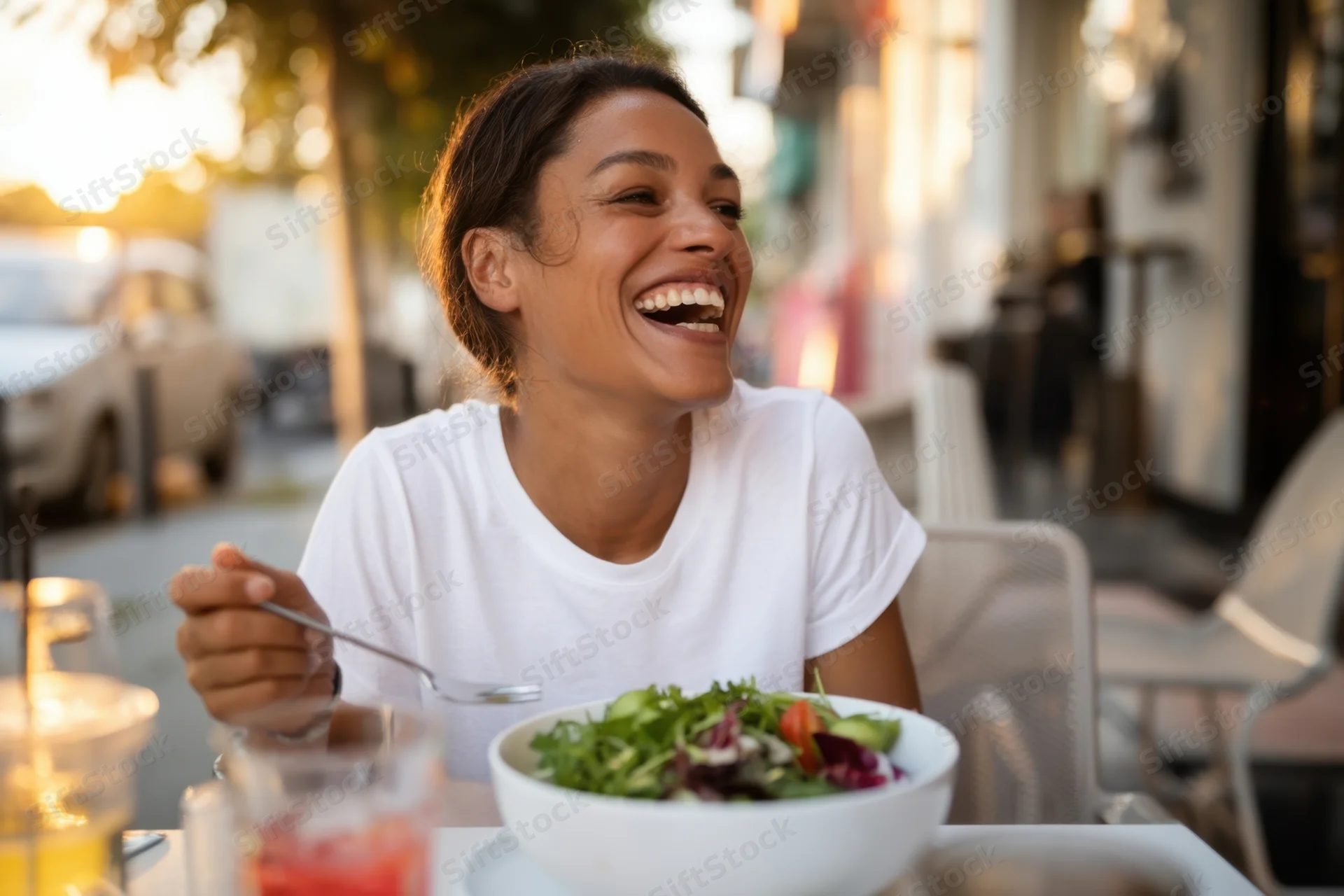 Woman laughing while holding fork over salad bowl at outdoor cafe table