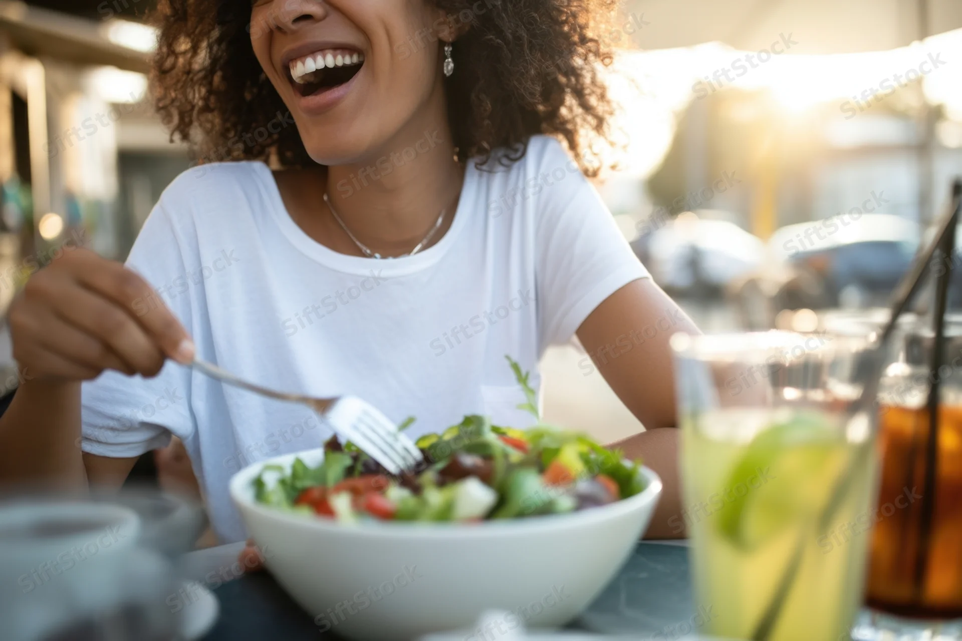 Woman laughing while eating salad at outdoor cafe table