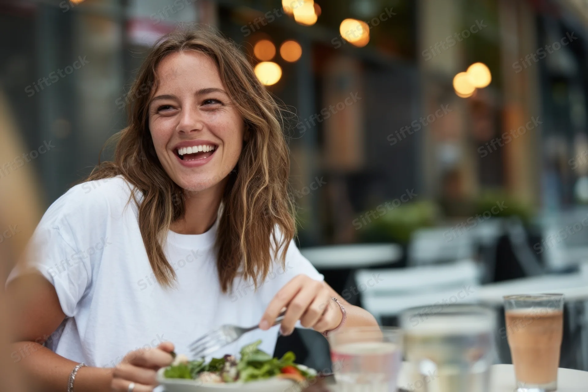Woman laughing while eating salad at outdoor cafe table