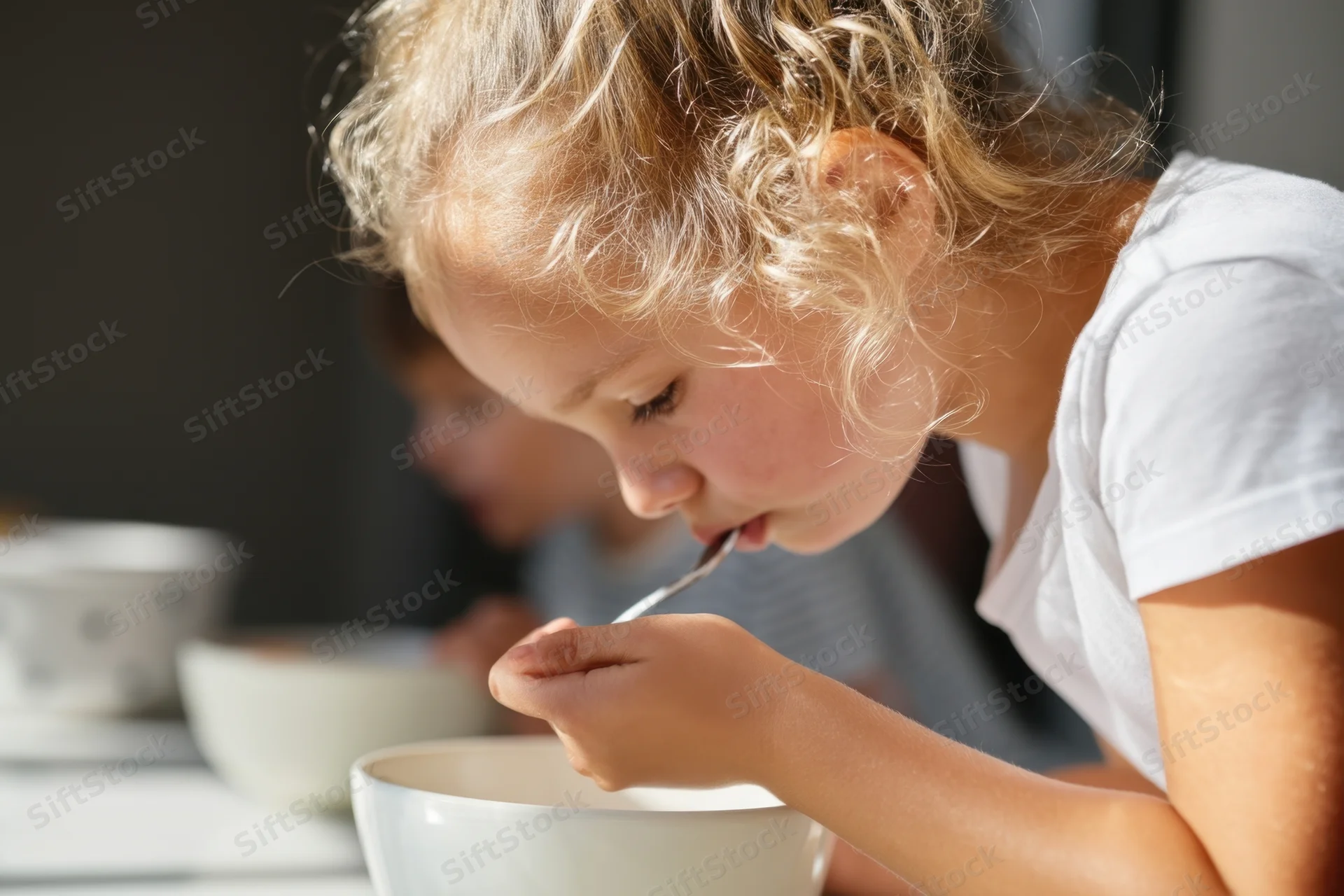 Young blonde girl eating cereal from a bowl at a kitchen table