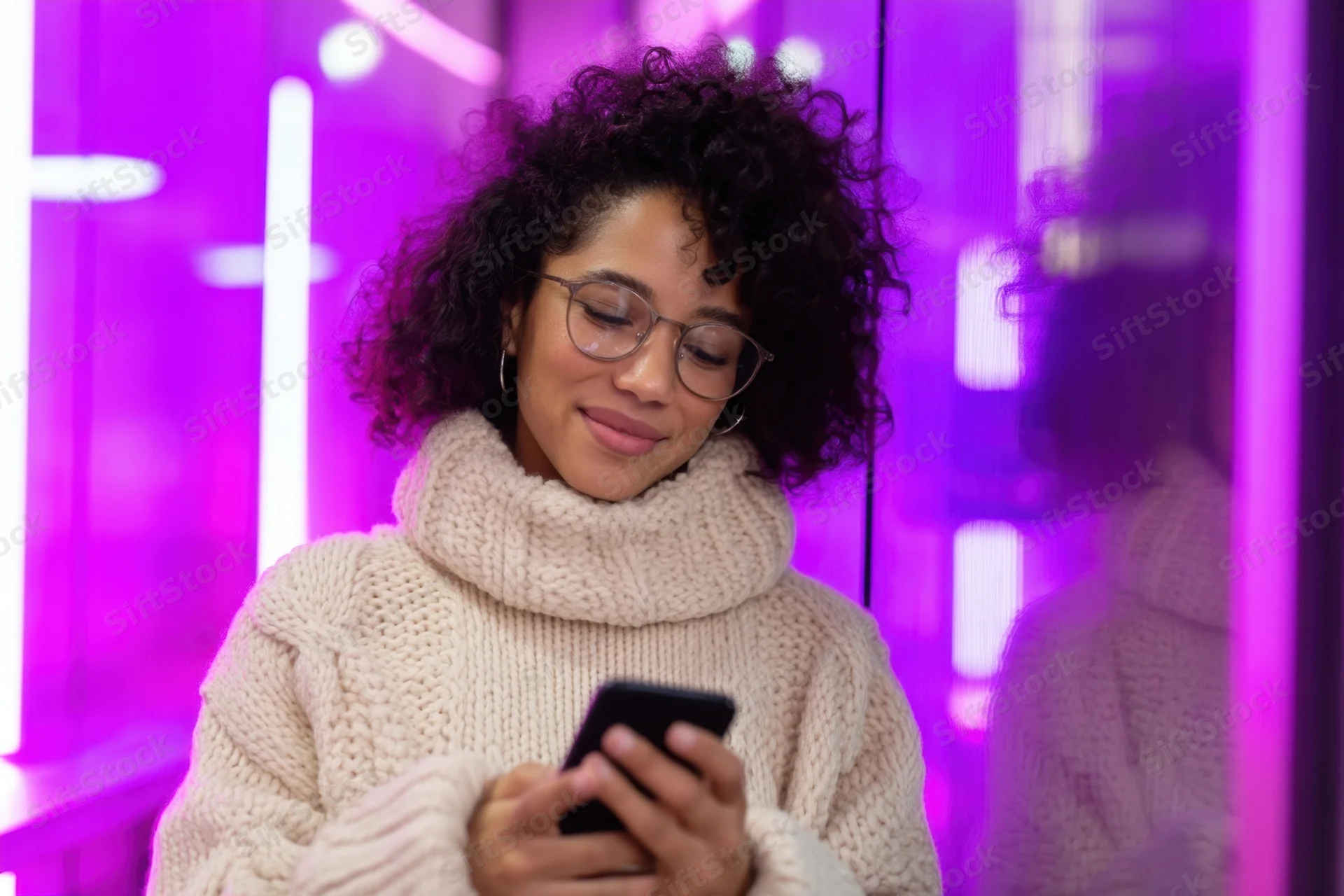 Young woman smiling while using smartphone in neon-lit urban interior