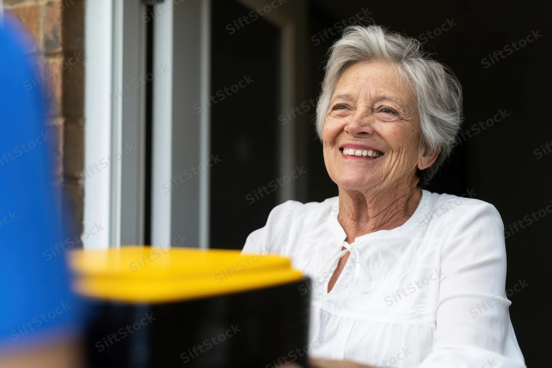 Elderly woman smiling in white blouse indoors near doorway