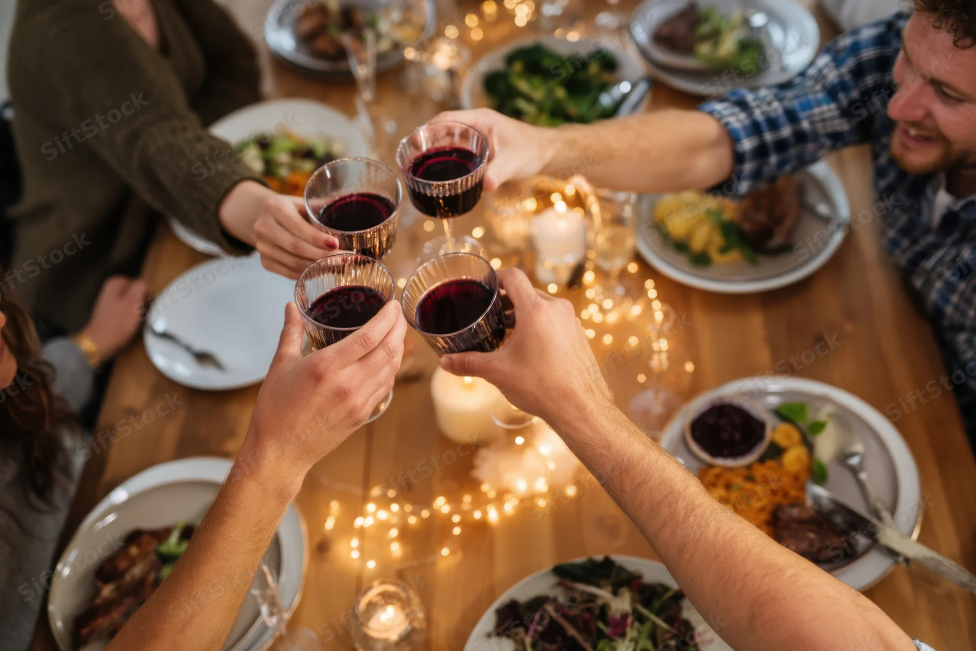 Hands raising wine glasses in a toast over a dinner table set with food and candles