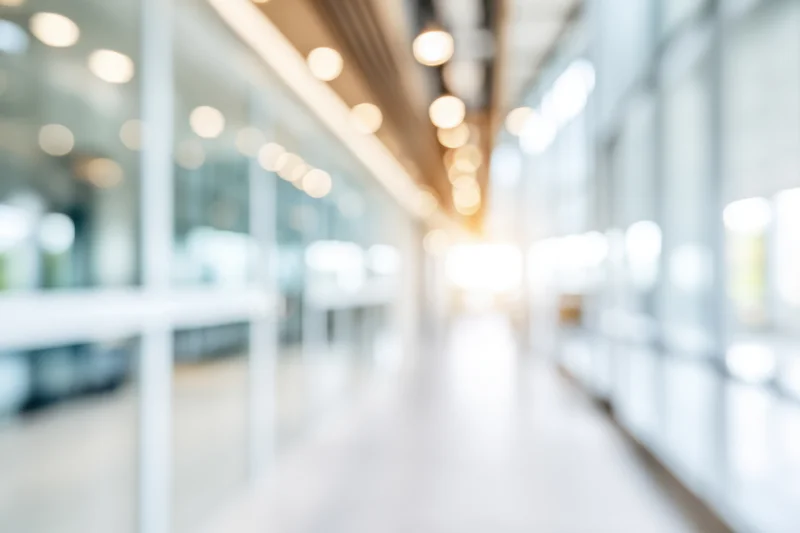 Blurred modern office corridor with glass walls and bright natural light