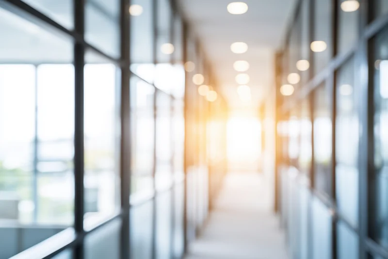Blurred modern office corridor with glass walls and bright natural light
