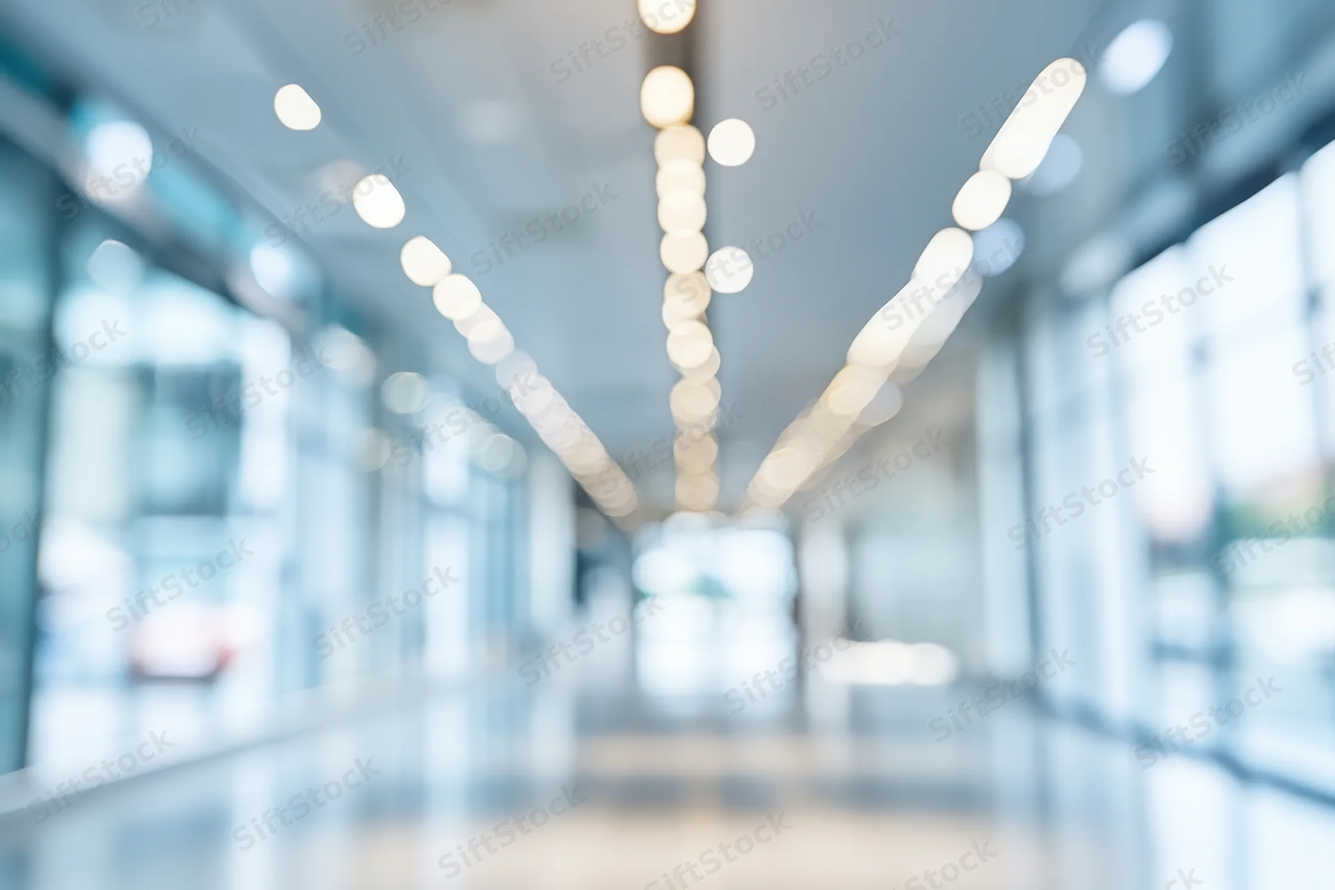 Blurred modern office corridor with glass walls and ceiling lights creating bokeh effect