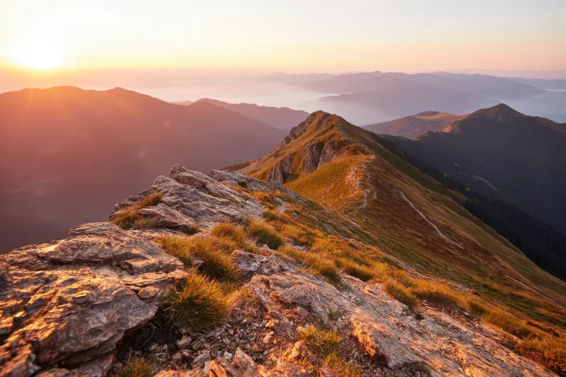 Mountain peak at sunset with rocky ridge and distant valley under golden sky