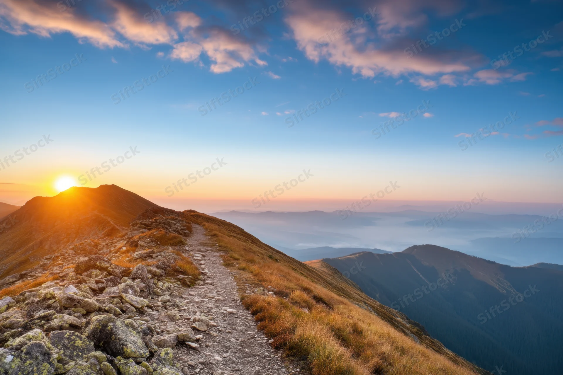 Mountain trail winding along a ridge at sunset with distant valley below