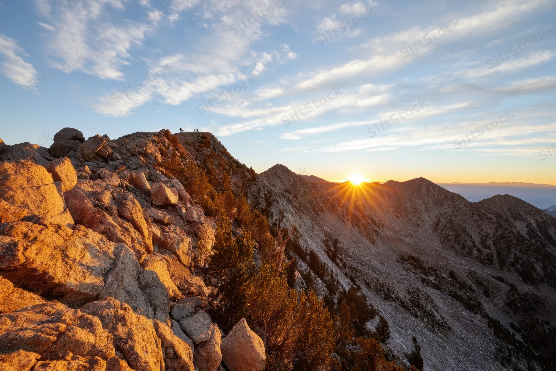 Sunrise over rugged mountain peak with hikers on summit and valley below