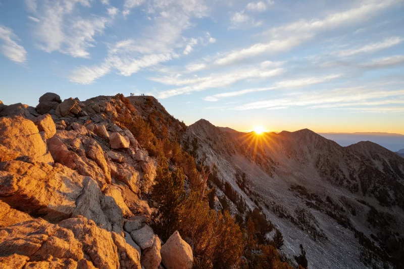 Sunrise over rugged mountain peak with hikers on summit and valley below