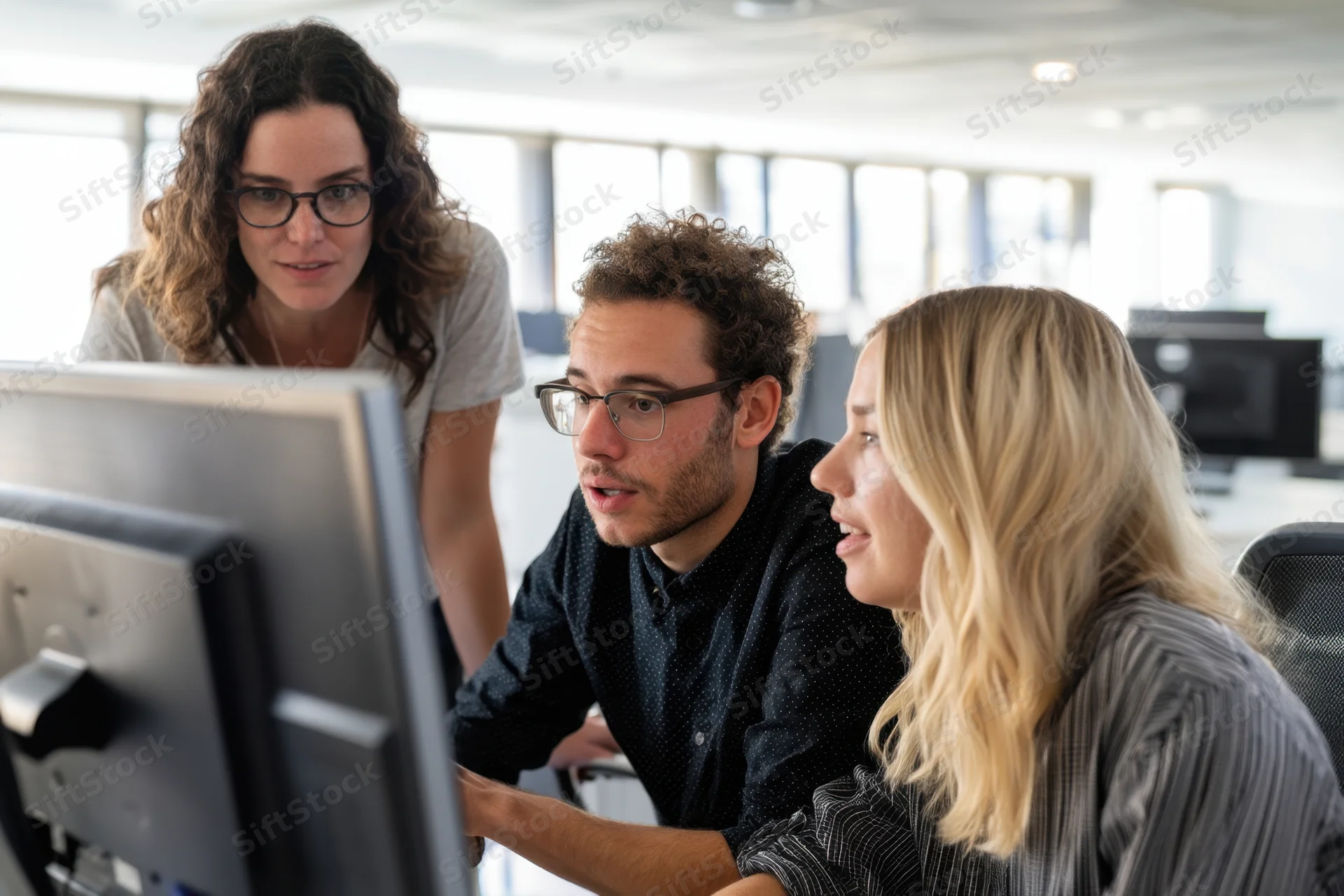 Three colleagues collaborating around a computer in a bright modern office