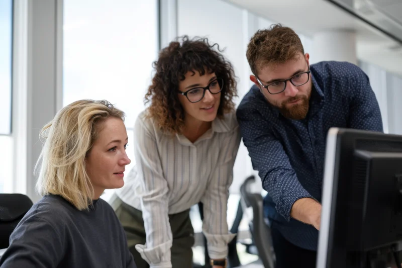 Three colleagues collaborating around a computer in a bright office