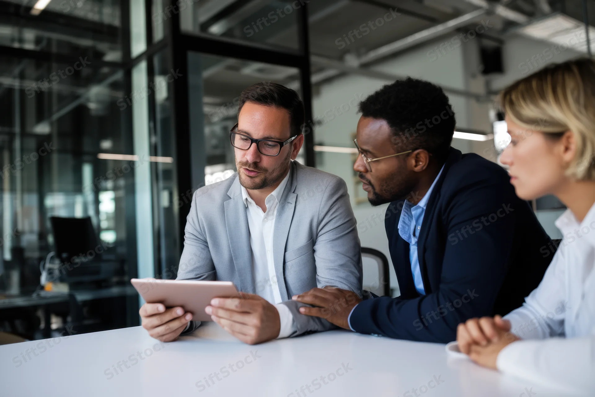 Three professionals collaborating around a white table in a modern office using a tablet