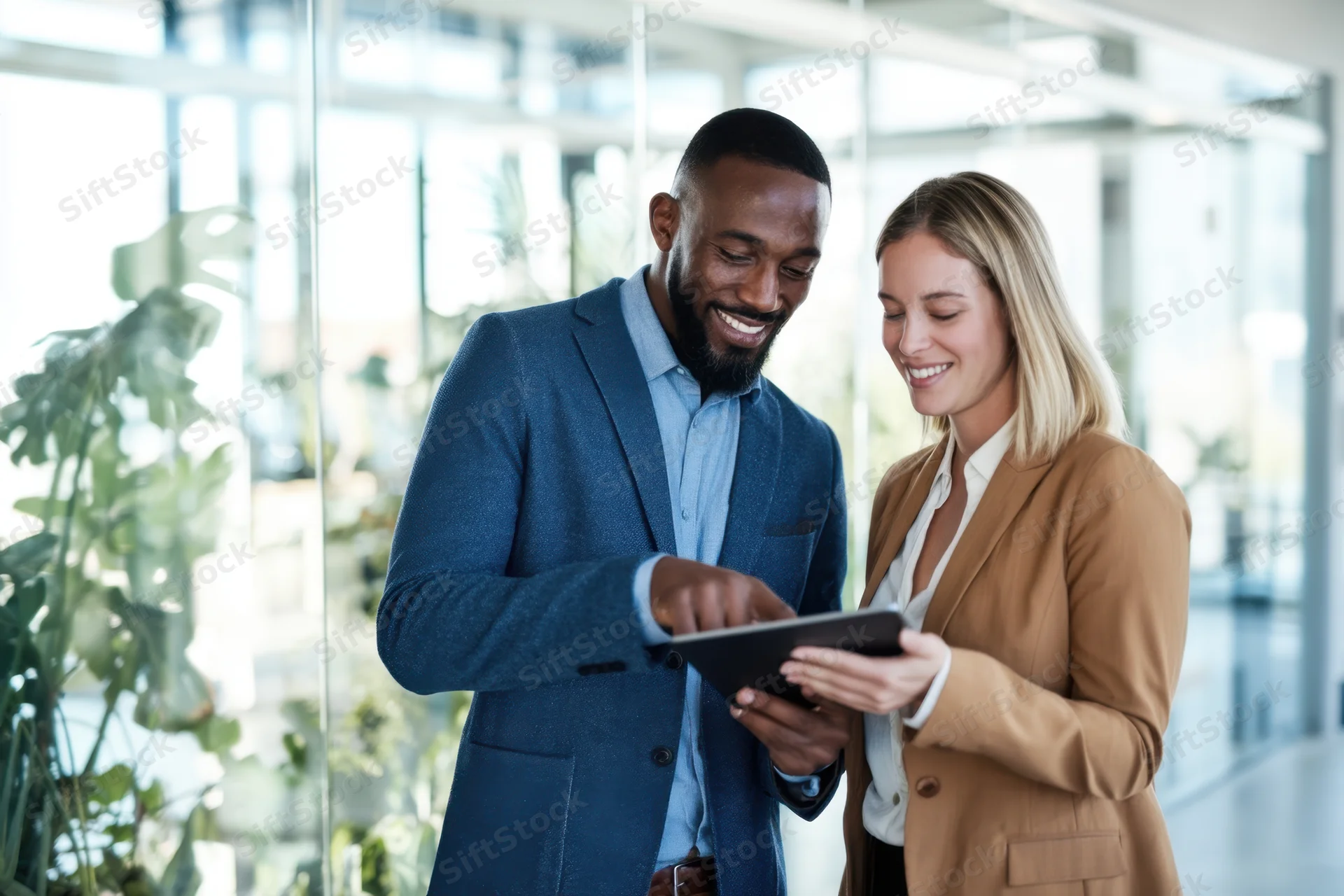 Two business professionals smiling while reviewing a tablet together in a bright modern office
