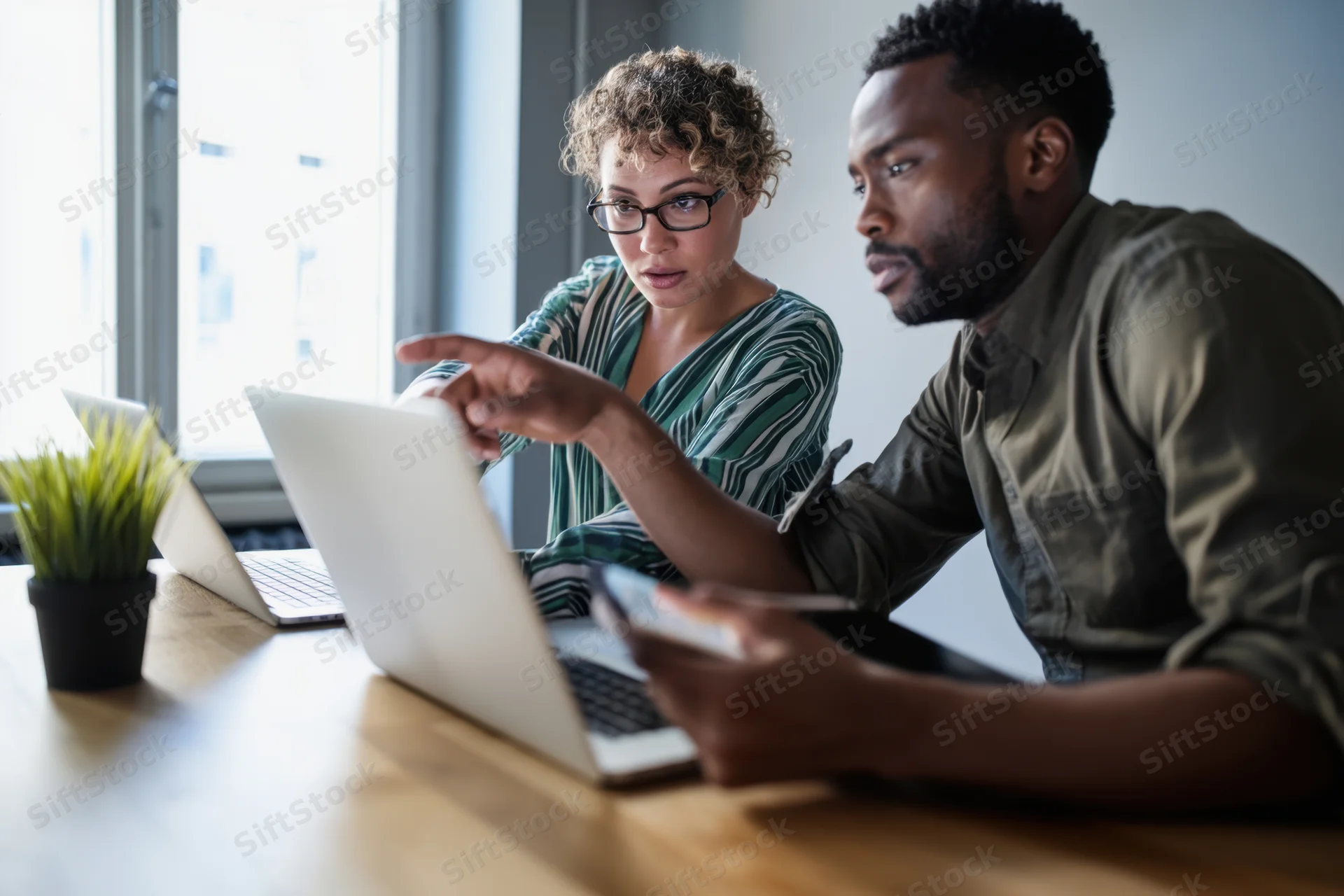 Two colleagues collaborating on laptops at a wooden desk in an office setting