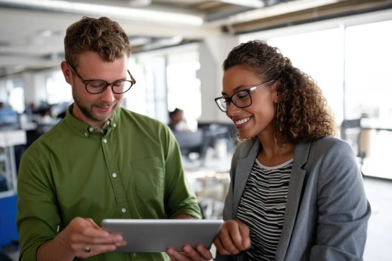 Two coworkers reviewing content on a tablet in a bright open-plan office