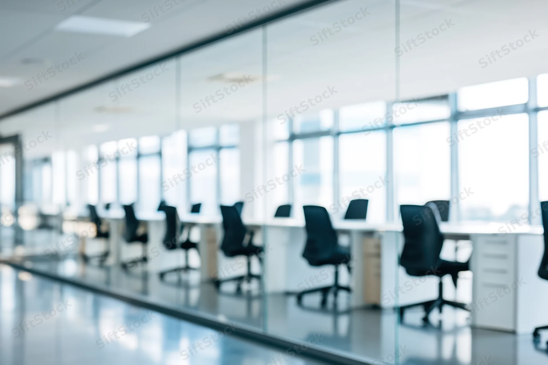 Modern office conference room with glass walls and desks arranged in a row along a windowed wall