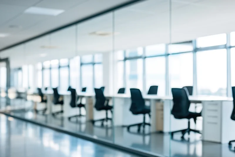 Modern office conference room with glass walls and desks arranged in a row along a windowed wall