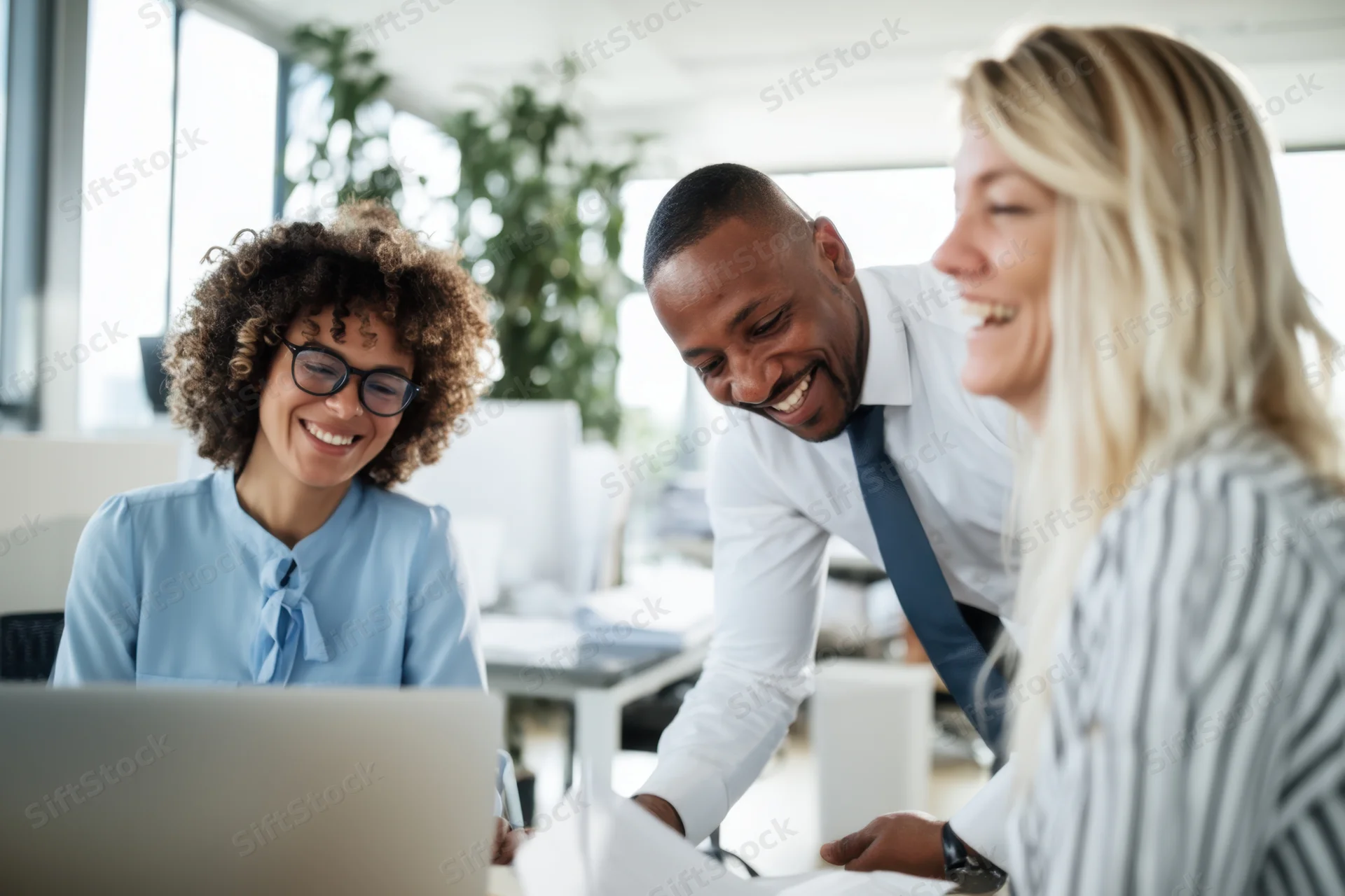 Three professionals laughing together over a laptop in a modern office
