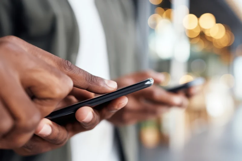 Close-up of hands holding and using smartphones in a modern urban setting with blurred city lights in the background