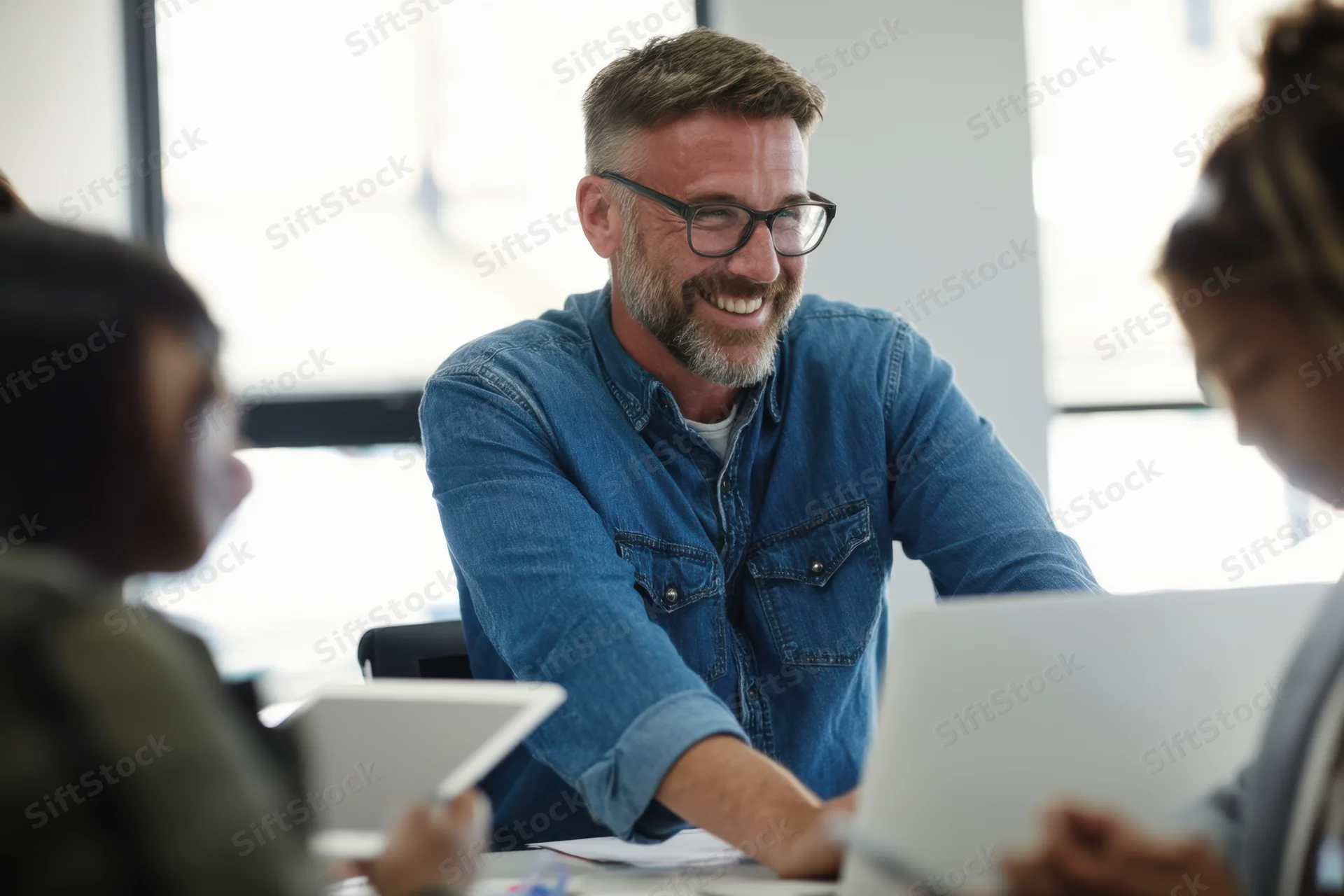 Man smiling during team meeting in bright office with colleagues around table