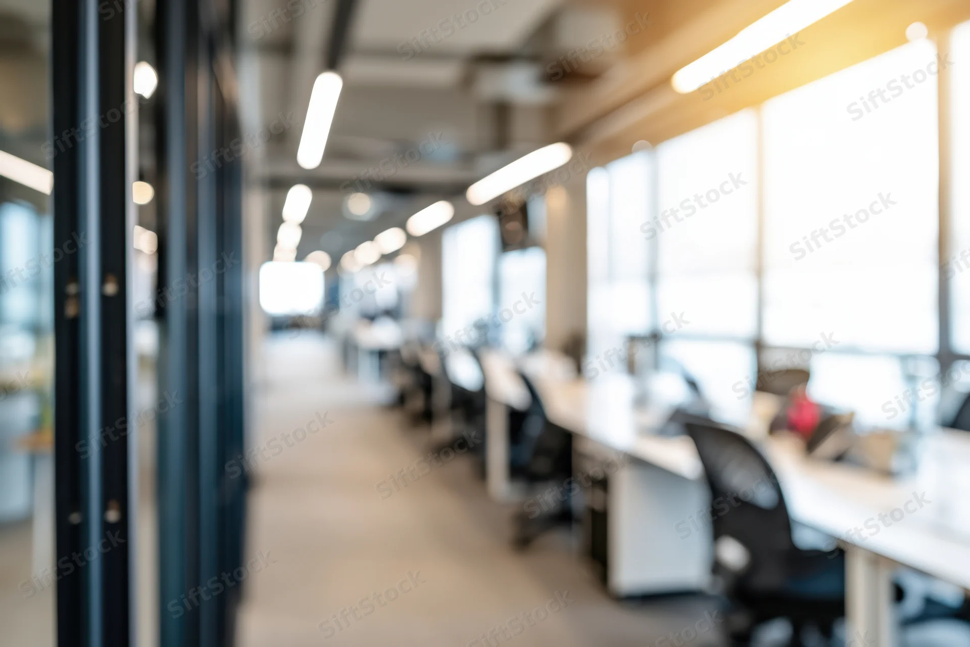 Blurred view of open-plan office interior with desks and chairs in a row along a hallway