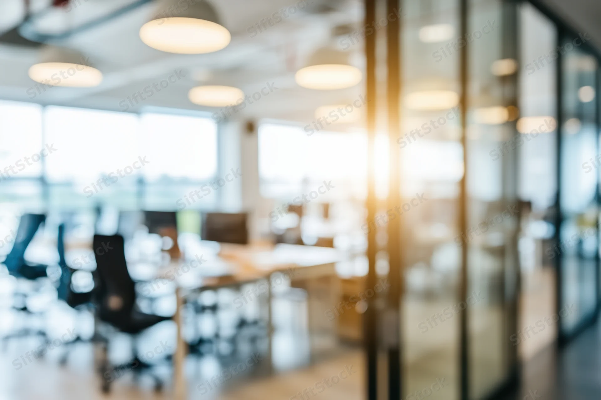 Blurred view of modern open-plan office interior with glass partitions and warm lighting