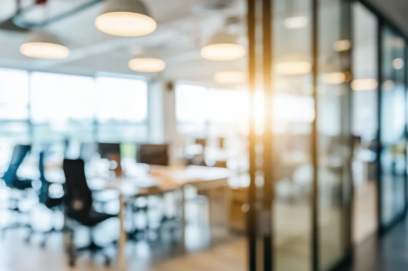 Blurred view of modern open-plan office interior with glass partitions and warm lighting