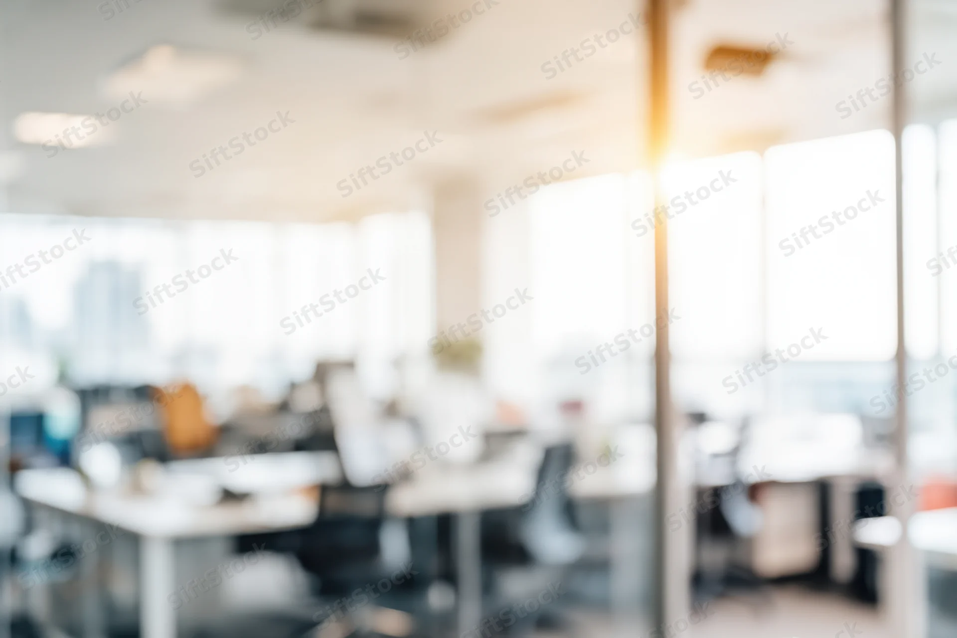 Blurred view of bright open-plan office interior with desks and chairs near windows