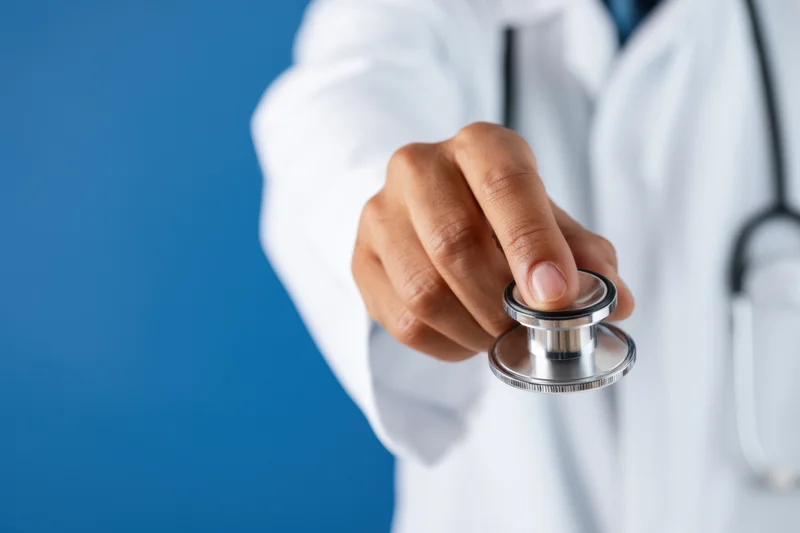 Doctor holding stethoscope extended forward against blue background
