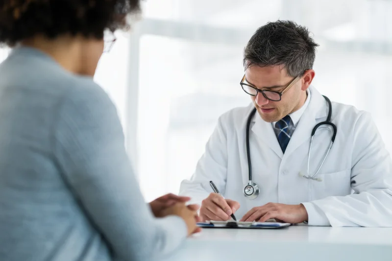 Doctor writing notes on clipboard during patient consultation in clinic office