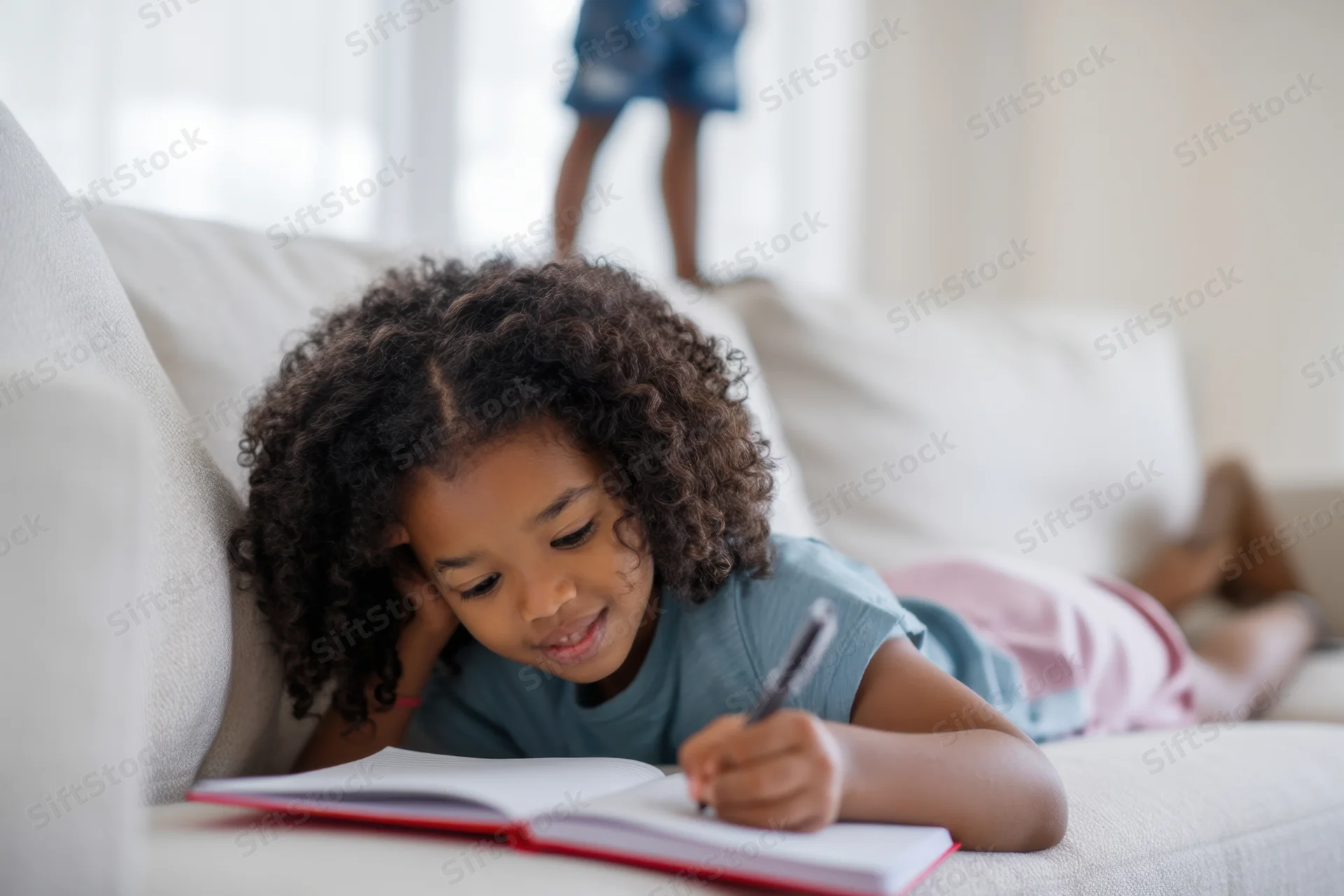 Girl lying on sofa writing in notebook at home