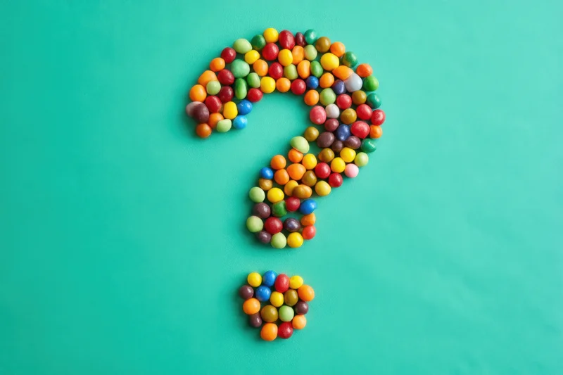 Question mark formed from multicolored round candies on turquoise surface