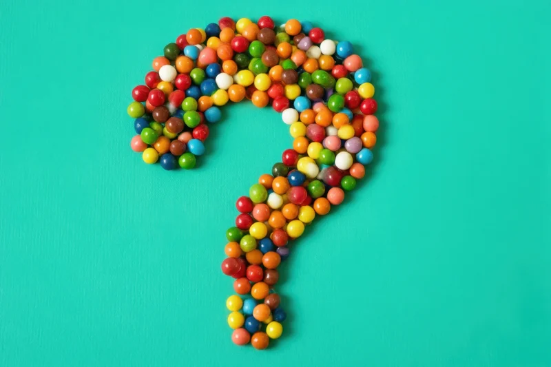 Question mark formed from multicolored round candies on turquoise surface