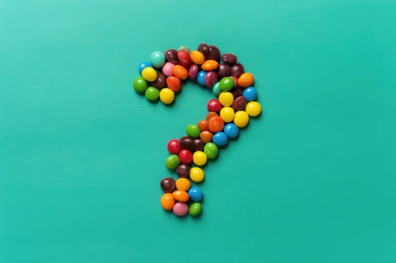 Multicolored round candies arranged in a question mark shape on a turquoise surface