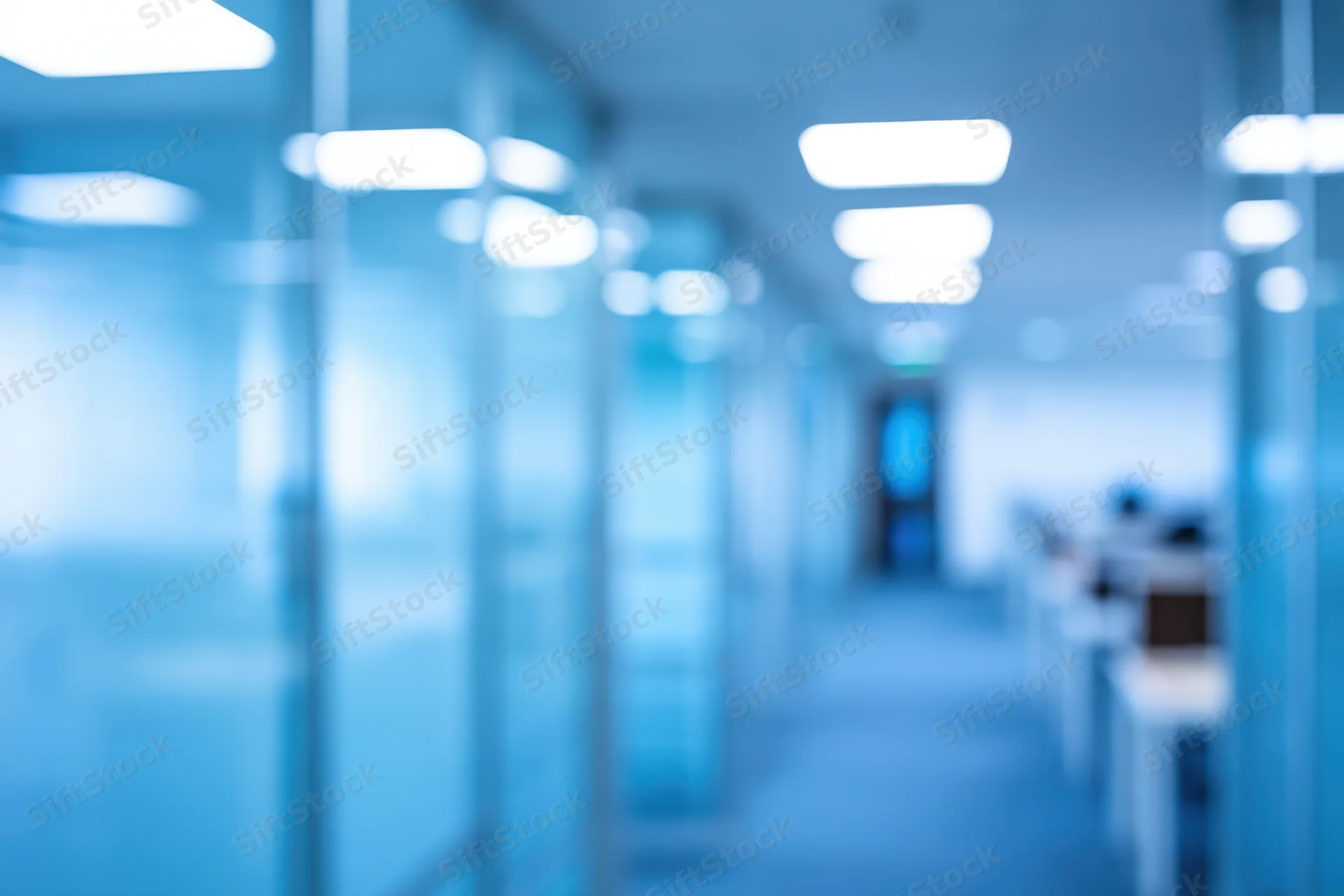 Blurred view of a modern office corridor with glass partitions and blue lighting