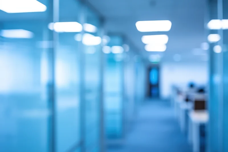 Blurred view of a modern office corridor with glass partitions and blue lighting