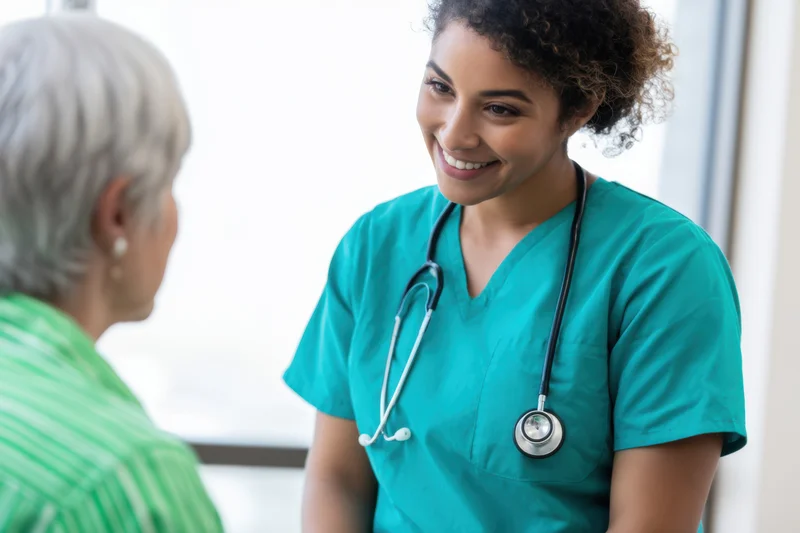 Nurse in teal scrubs smiling while consulting with a senior patient in a clinic