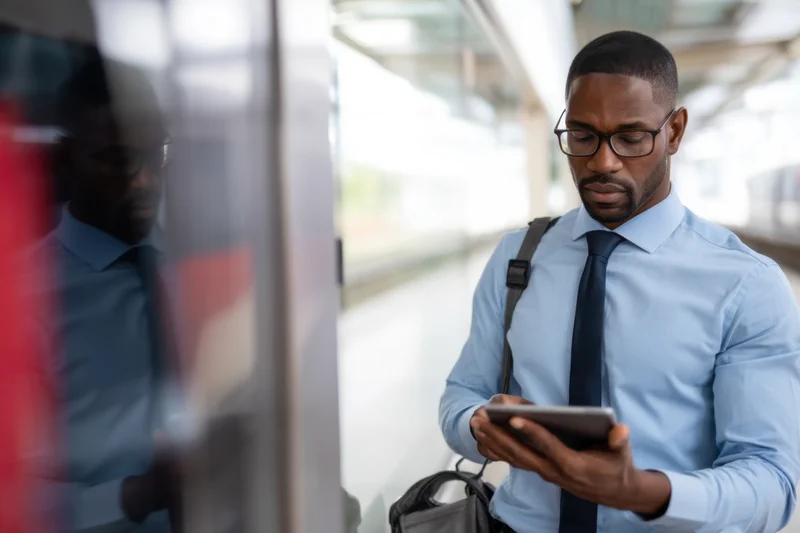 Man in business attire using smartphone while waiting on train platform