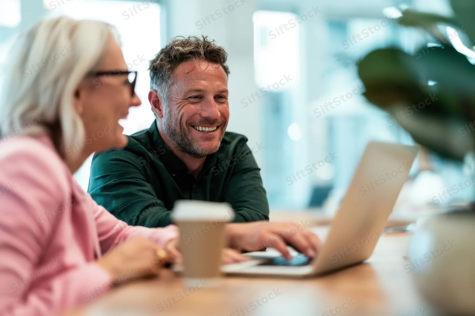 Man and woman smiling while working on laptop together at office desk