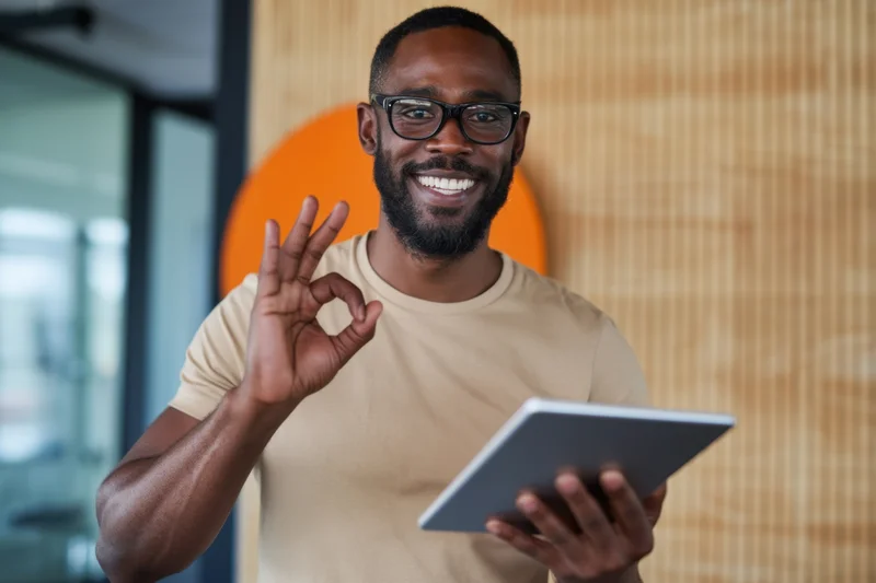 Smiling man making ok gesture with tablet in modern office