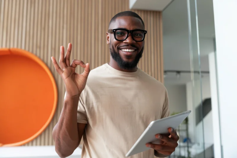Smiling man making ok gesture with tablet in modern office interior