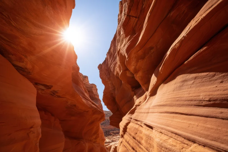 Sunlit slot canyon with smooth orange-red sandstone walls under blue sky