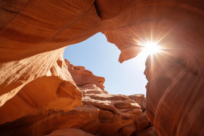 Sunlit slot canyon with smooth orange-red sandstone walls and sky visible through opening