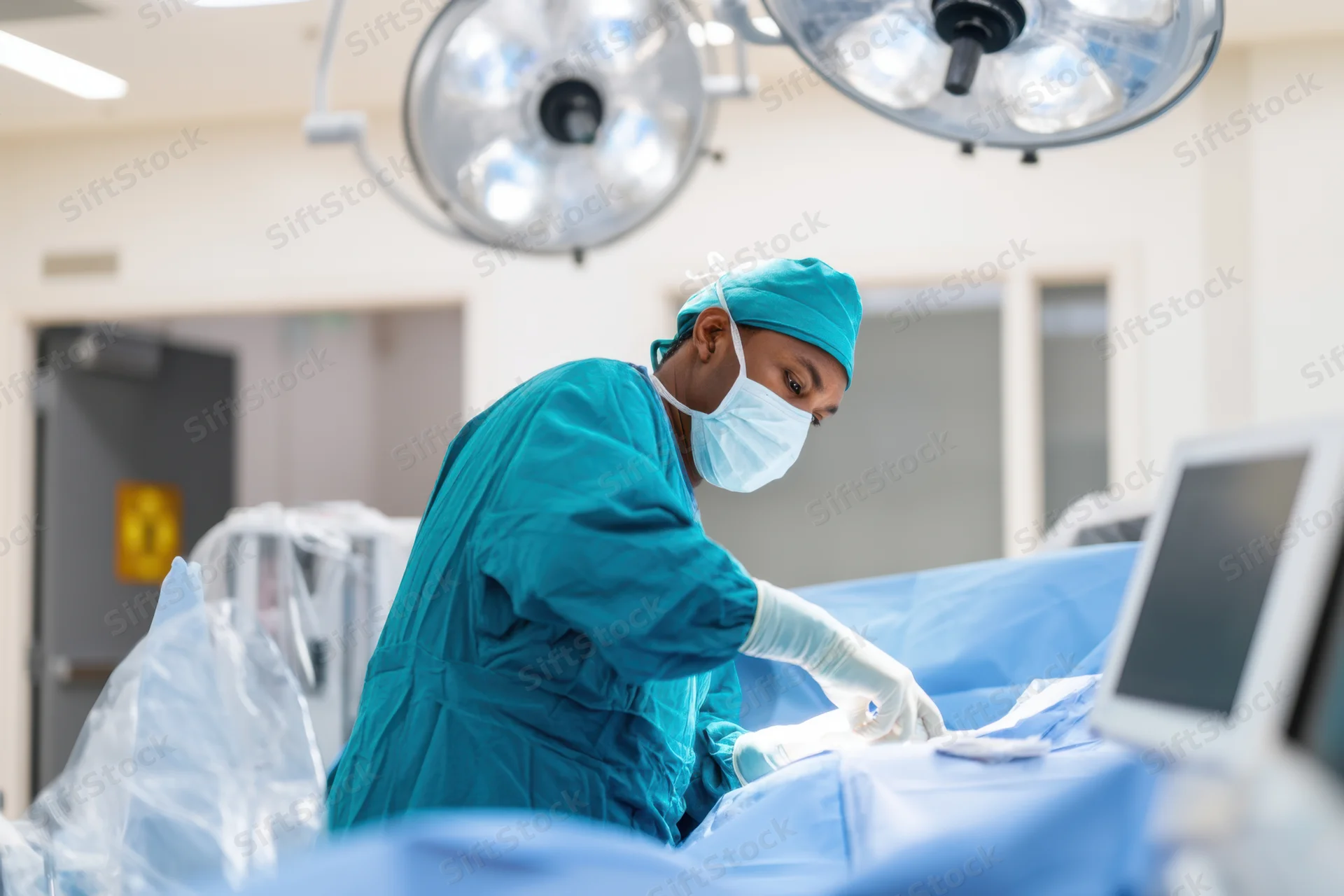 Surgeon performing surgery in an operating room with surgical drapes and monitors visible