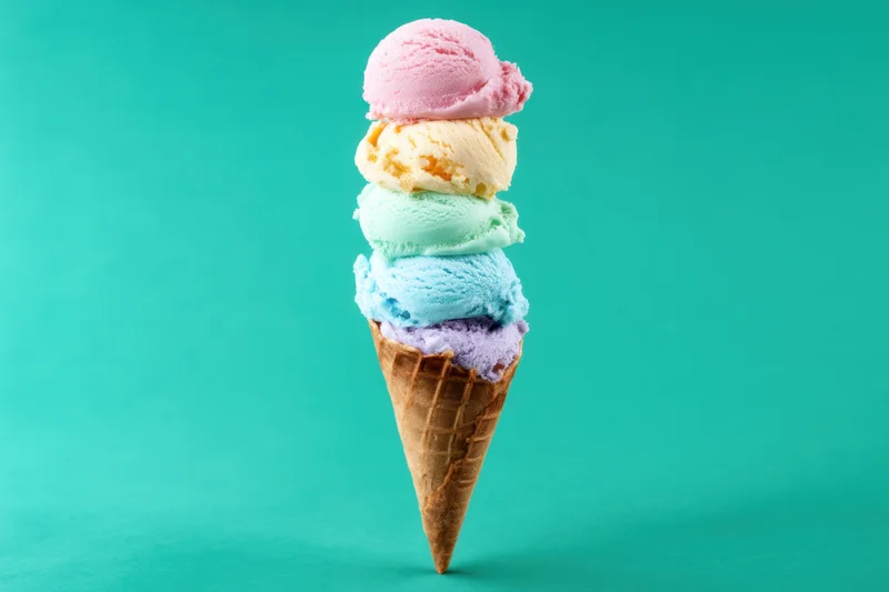 Tall waffle cone stacked with five colorful ice cream scoops against a teal background
