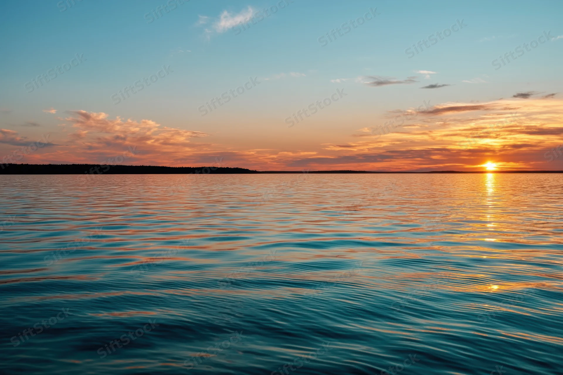 Sunset over a calm lake with rippling water reflecting golden light on the horizon