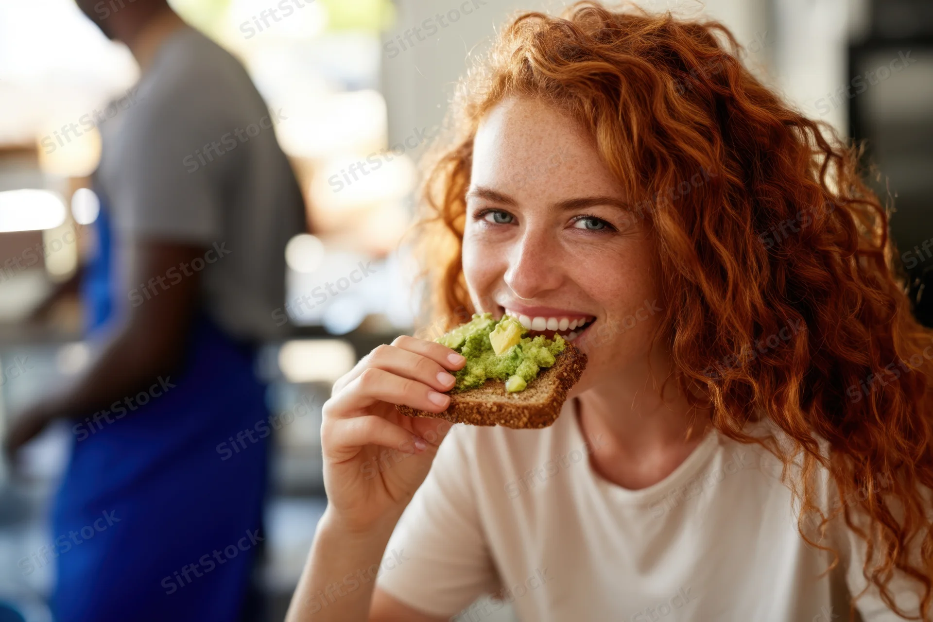 Woman smiling while eating avocado toast in a cafe